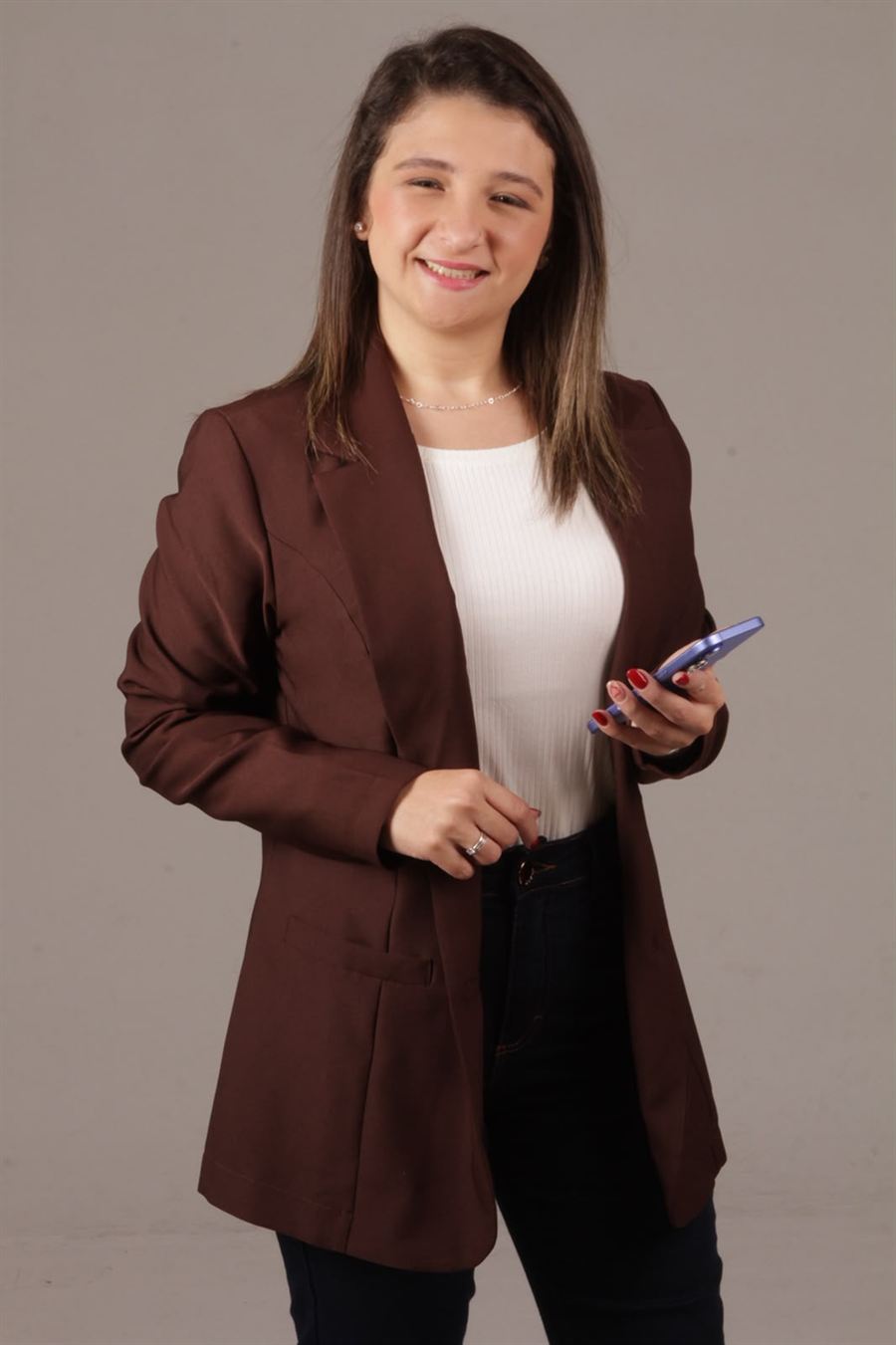 Bruna Fernandes sorrindo, de blazer marrom, com o celular na mão
